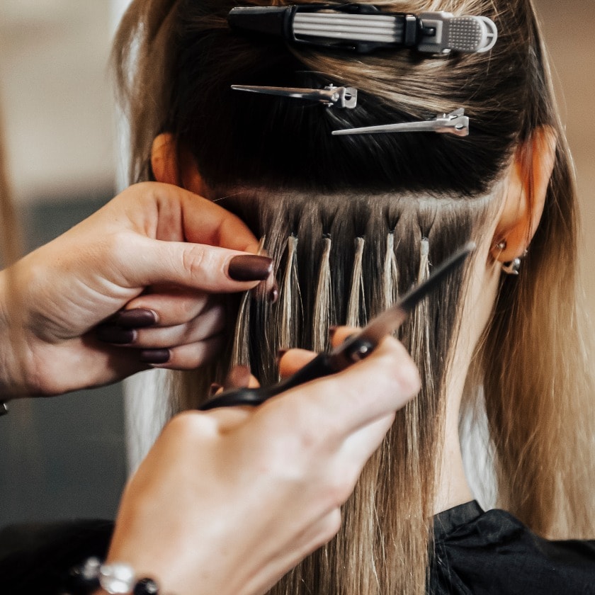 The hairdresser does hair extensions to a girl, a blonde in a beauty salon. Professional hair concept